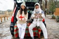 Young couple giving presents and looking at camera sitting in the trunk in winter holidays. Royalty Free Stock Photo