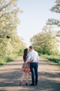 Beautiful young couple holding hands and walking on road in sunshine among spring field and trees. Happy family in love relaxing Royalty Free Stock Photo