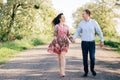 Beautiful young couple holding hands and walking on road in sunshine among spring field and trees. Happy family in love relaxing Royalty Free Stock Photo