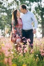 Beautiful young couple holding hands and walking in sunshine in spring meadow with pink flowers. Happy family smiling in green Royalty Free Stock Photo