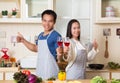 Beautiful young couple is holding wine and thumbs up while cooking in kitchen at home Royalty Free Stock Photo