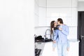 Beautiful young couple is hugging and smiling while drinking tea or coffee in kitchen at home. Man is kissing his charming girl Royalty Free Stock Photo