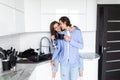 Beautiful young couple is hugging and smiling while drinking tea or coffee in kitchen at home. Man is kissing his charming girl Royalty Free Stock Photo