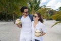 Beautiful young couple joyfully on a tropical beach with coconuts in their hands on the seashore under a green palm tree. Royalty Free Stock Photo