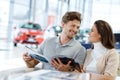 Beautiful young couple looking a new car at the dealership showroom.