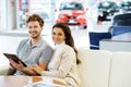 Beautiful young couple looking a new car at the dealership showroom. Royalty Free Stock Photo