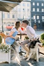 Beautiful young couple in love enjoying summer walk in the city street with their husky dogs, sitting at the table in