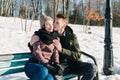 Beautiful young couple in love sitting on a park bench on a clear sunny winter day. Boy embraces and kiss his girlfriend Royalty Free Stock Photo