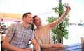 Beautiful young couple is making selfie using a smartphone and smiling while sitting in the cafe. Royalty Free Stock Photo