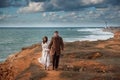 Beautiful young couple bearded man in coat holding his woman with hair blown with wind walking along brown sea coast with