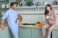 Beautiful young couple in pajamas is looking at each other and smiling while cooking in kitchen at home Royalty Free Stock Photo