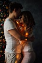 Beautiful young couple in pajamas on nicely decorated Christmas tree background.