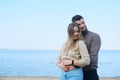 Beautiful young couple posing on the beach against the backdrop of a large lake. Man hugging woman from behind and Royalty Free Stock Photo