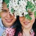 Beautiful young couple posing and smiling under white flowers in spring garden. Portraits of happy family embracing at blooming Royalty Free Stock Photo