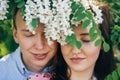 Beautiful young couple posing and smiling under white flowers in spring garden. Portraits of happy family embracing at blooming Royalty Free Stock Photo