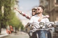 Beautiful young couple riding scooter together while happy woman pointing away and smiling. toned Royalty Free Stock Photo