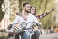 Beautiful young couple riding scooter together while happy woman pointing away and smiling. toned Royalty Free Stock Photo