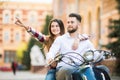 Beautiful young couple riding scooter together while happy woman pointing away and smiling Royalty Free Stock Photo