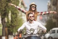 Beautiful young couple riding scooter together while happy woman raising arms and smiling Royalty Free Stock Photo