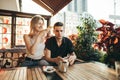 Beautiful young couple sitting on terrace at restaurant at sunset and drinking coffee, happy girl taking photo on smartphone Royalty Free Stock Photo