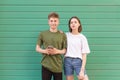 Beautiful young couple standing on the background of a green wall in the headphones, looking at the camera. Nice guy and a girl