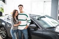 Beautiful young couple standing at the car dealership and making their decision