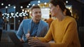 Beautiful Young Couple is Using a Laptop while Sitting at a Table in an Outdoors Street Food Cafe. Royalty Free Stock Photo