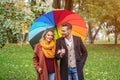 A beautiful young couple is walking in the park under a rainbow colored umbrella. A beautiful girl walks through the Royalty Free Stock Photo