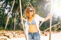 Beautiful young curly funny girl on a swing on a tropical beach, freedom, vacation, travel, joy and happiness concept