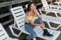 Beautiful young curly woman in denim clothes with yellow fashion top blouse, classic blue jeans and leather shoes sits on sunbed Royalty Free Stock Photo