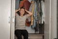 Beautiful young curly woman does not know what to wear, sits in a closet with clothes in sadness and depression Royalty Free Stock Photo