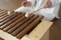 Beautiful young curly woman playing on a wooden xylophone sitting on the floor in white clothes