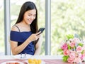 A beautiful young cute black long hair Asian woman sitting in a restaurant with sweet color bouquet and using smartphone with Royalty Free Stock Photo