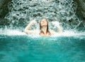 Beautiful young cute redhead woman in Bikini under the splashing water of the waterfall in the Spa Wellness pool and raises her Royalty Free Stock Photo