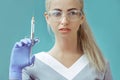 Beautiful young doctor in medical robe holding syringe with liquid. Isolated over blue background, Royalty Free Stock Photo