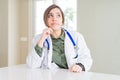 Beautiful young doctor woman wearing medical coat and stethoscope with hand on chin thinking about question, pensive expression Royalty Free Stock Photo