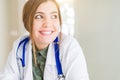 Beautiful young doctor woman wearing medical coat and stethoscope smiling looking side and staring away thinking Royalty Free Stock Photo