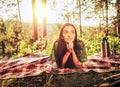 Beautiful young dreaming girl lying on a plaid in a forest glade during sunset bright sunlight around beauty of nature