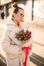 Beautiful young dreamy woman with fresh spring tulips flowers bouquet at city street Royalty Free Stock Photo