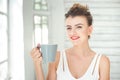 Beautiful young European woman enjoying a cup of coffee or tea while relaxing in Bright white room. Royalty Free Stock Photo