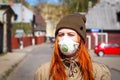 Beautiful young European woman with ginger coloured hair on the street with a medical face mask on