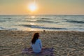 Beautiful young european woman sitting on the beach near ocean during sunset Royalty Free Stock Photo