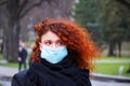 Beautiful young European woman in spring clothes on the street with a medical face mask on. Royalty Free Stock Photo