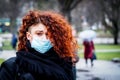 Beautiful young European woman in spring clothes on the street with a medical face mask on. Royalty Free Stock Photo