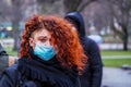 Beautiful young European woman in spring clothes on the street with a medical face mask on Royalty Free Stock Photo