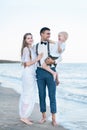 Beautiful young family of three walking along the sea shore. Father holds child on hands. Vertical frame Royalty Free Stock Photo