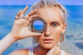 Beautiful young fashion model on the beach. Close up portrait of boho model holding small mirror at her eye