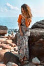 Beautiful young fashionable woman in elegant dress posing at the stone beach at sunset Royalty Free Stock Photo