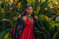 Beautiful young fashionable woman with make up and stylish boho accessories posing on natural tropical background