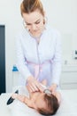 Beautiful young female blonde pediatrician doctor examines baby girl with stethoscope checking heart beat. baby is lying on the